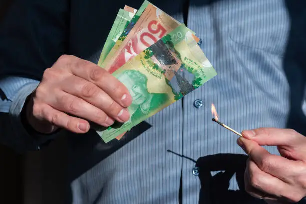 Photo of Close-up of man's hands holding burning match near Canadian dollars