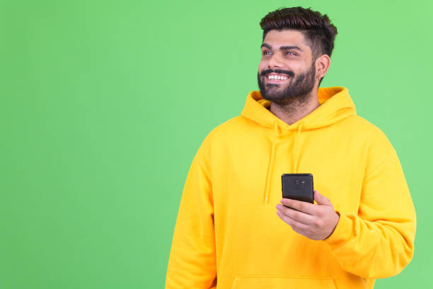 istock Happy young overweight bearded Indian man thinking while using phone 1196753030