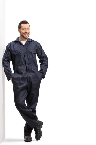 Male worker in an overall uniform leaning on wall Full length portrait of a male worker in an overall uniform leaning on wall isolated on white background jumpsuit stock pictures, royalty-free photos & images