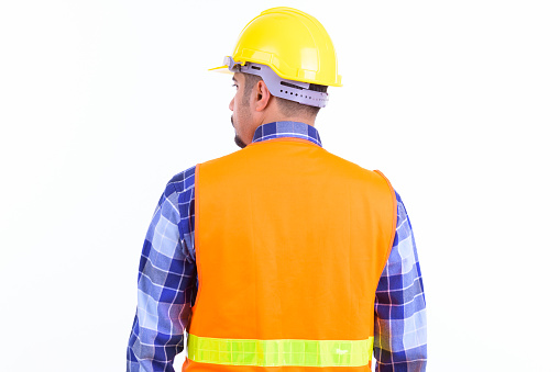 Studio shot of young handsome bearded Iranian man construction worker isolated against white background