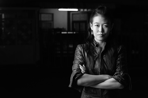 Portrait of beautiful Asian rebellious woman wearing leather jacket in the streets outdoors at night in black and white