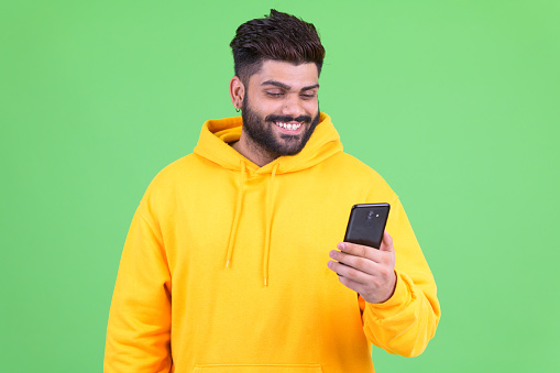 Studio shot of young overweight bearded Indian man wearing hoodie against chroma key with green background