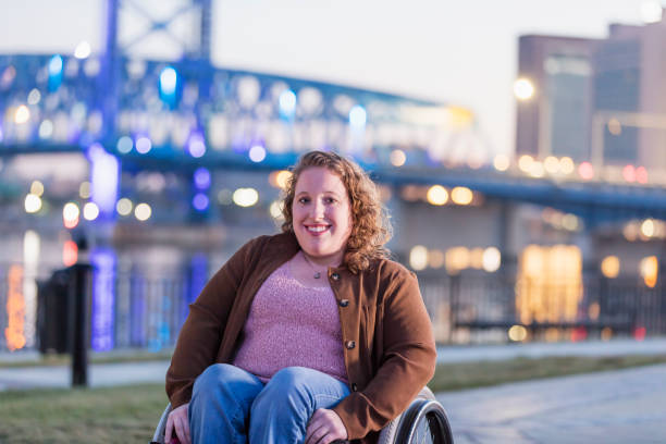mujer con espina bífida en silla de ruedas en el paseo marítimo de la ciudad - physical impairment smiling front view looking at camera fotografías e imágenes de stock