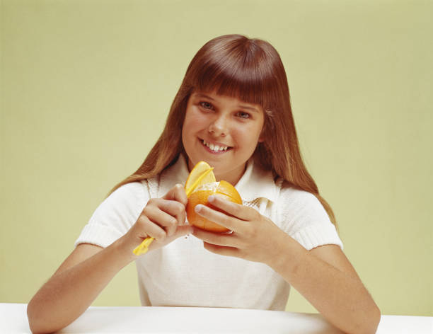 teenager mädchen peeling orange, lächeln, porträt - 70er jahre frisur stock-fotos und bilder