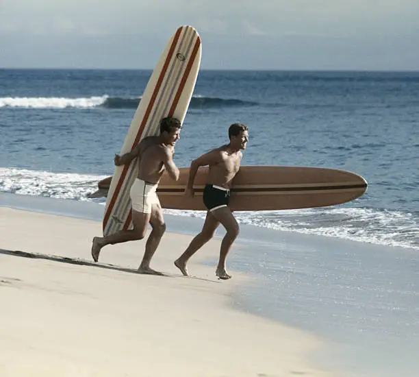 Photo of Young men running on beach with surfboard