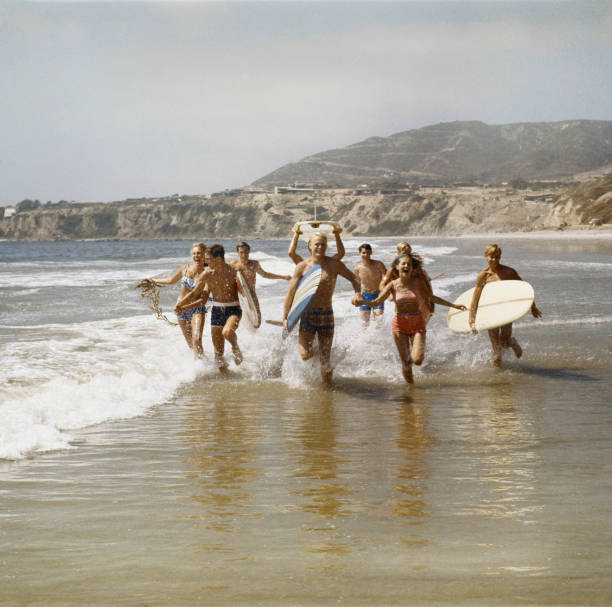groupe de surfers courant dans l'eau avec des planches de surf, souriant - horizontal men women surfboard photos et images de collection