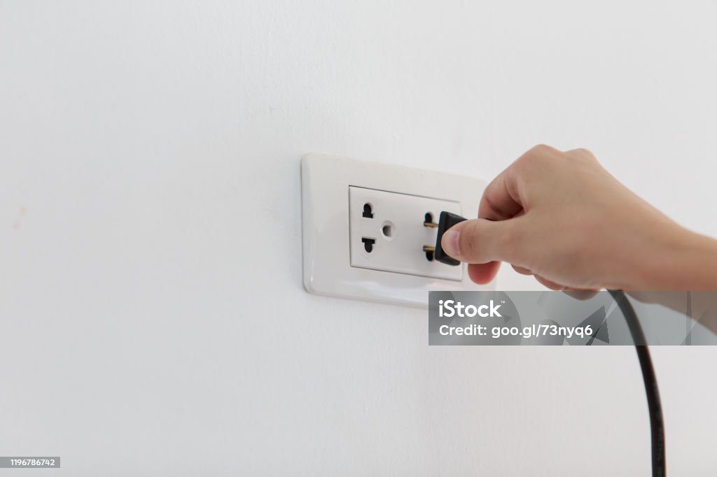 Hand Putting Plug Into Electricity Socket on clean cement plaster wall background. Unplug or plugged and pull electric plug Outlet Store Stock Photo