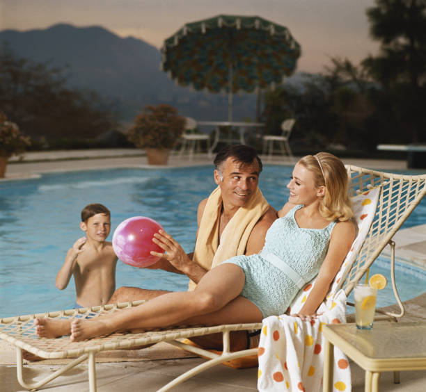 Father and son playing with beach ball while mother relaxing on lounge chair, smiling  1968 stock pictures, royalty-free photos & images