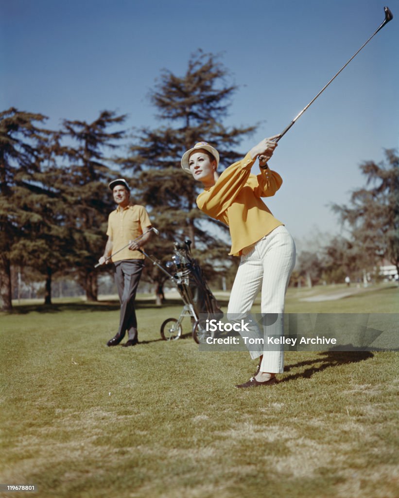 Jeune femme jouant au golf et homme debout à l'arrière-plan - Photo de D'archive libre de droits