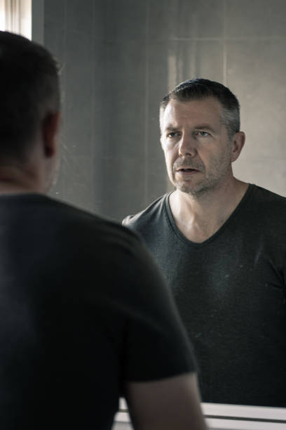 istock Man in a grey v-neck tshrt looking at himself in mirror with intense expression 1196788304
