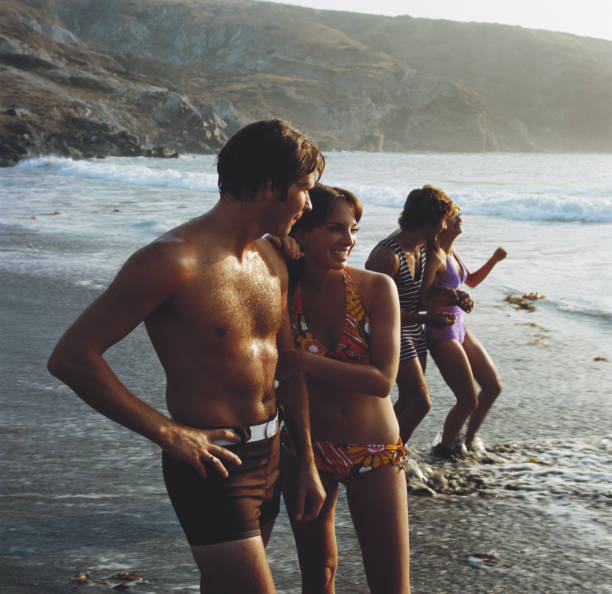 junge paare stehen am strand, die lächelnd - swimming trunks fotos stock-fotos und bilder