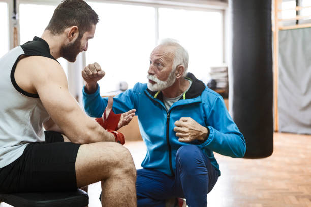 Young boxer listening senior trainer for pointers Young boxer training old man boxing stock pictures, royalty-free photos & images