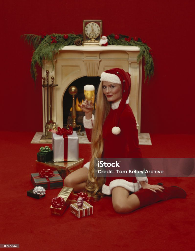 Young woman holding beer glass in front of fireplace, smiling, portrait  Archival Stock Photo