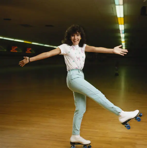 Photo of Young woman roller skating on wooden floor, smiling, portrait