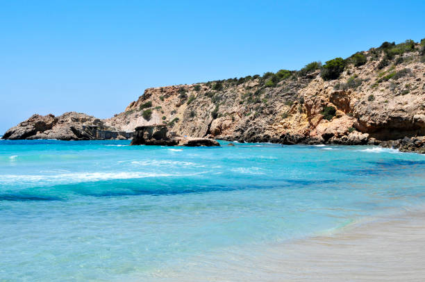 a view of the Mediterranean sea at Cala Tarida beach in Ibiza Island, Spain, with some traditional fishermen shelters in the background