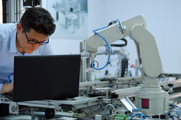 istock Close-up robotic arm. Engineer is working on laptop to programming smart factory automation and automated car on production line. Industry 4.0 concept; artificial intelligence in smart factory. 1196810813