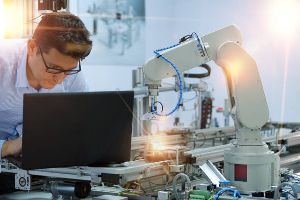 istock Close-up robotic arm. Engineer is working on laptop to programming smart factory automation and automated car on production line. Industry 4.0 concept; artificial intelligence in smart factory. 1196812654