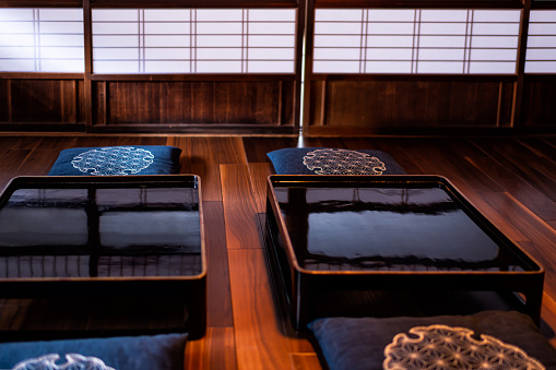 Traditional japanese machiya house or ryokan restaurant with two black lacquered wood tables and nobody closeup with pillow cushions by shoji door