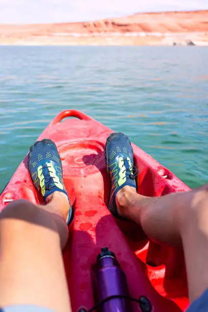 Kayaking in Lake Powell to antelope canyon with legs feet water shoes at front of red kayak boat and blue water