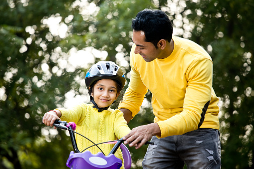 Girl learning to ride a bicycle with her father in park