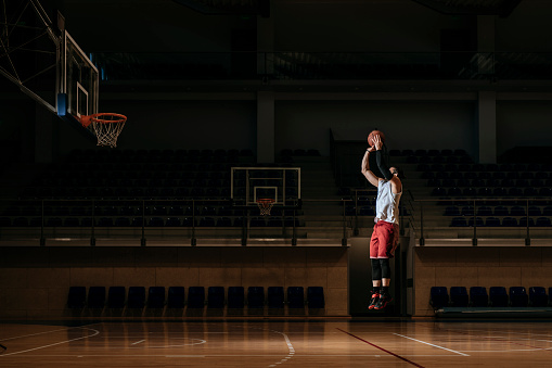 Basketball player standing alone on indoor court and shooting a ball.