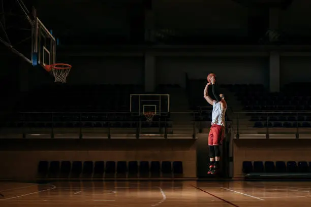 Basketball player standing alone on indoor court and shooting a ball.
