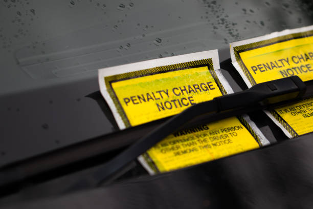 istock Two bright yellow parkings ticket tucked under the windscreen/windshield wiper. 1196822432