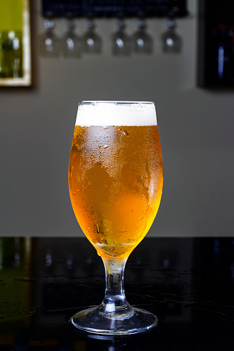 Glass full of beer, with pilsen beer or chopp, on a black table in a pub