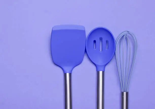 Set of tools for cooking on purple background. Silicone paddles with metal handles, whisk. Top view. Copy space."n