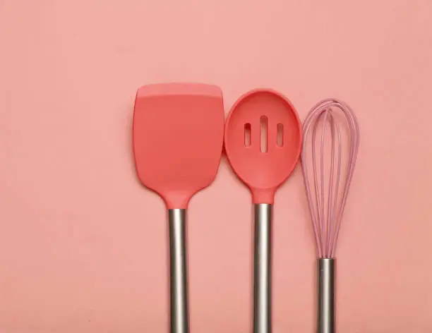 Set of tools for cooking on coral background. Silicone paddles with metal handles, whisk. Top view. Copy space."n