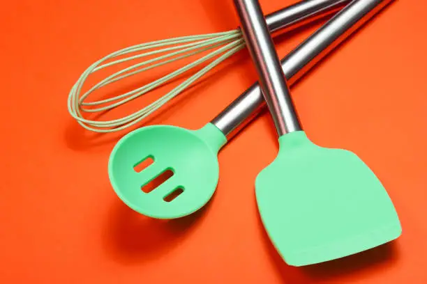 Set of tools for cooking on orange background. Silicone paddles with metal handles, whisk.