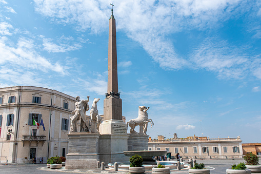 People walking next to the Quirinale obelisk in Rome, Italy. The Quirinale building holds the government authority in Rome, Italy.