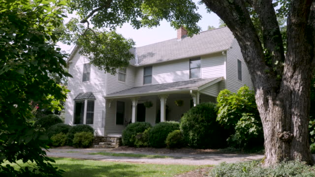 Establishing shot of a large two story house surrounded by large old trees