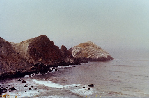 A long shot along the Big Sur, California coast, waves lapping along the beach on a foggy summer morning