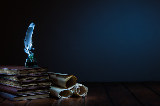 Quill pen and rolled papyrus sheets on a wooden table with old books