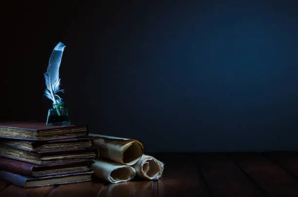 Quill pen and rolled papyrus sheets on a wooden table with old books