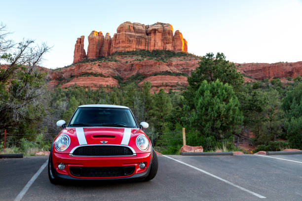 red mini cooper s with white stripes parked in front of cathedral rock in sedona arizona as the sun is setting over the red rock cliffs with landscape crop - usa scenics sedona photography imagens e fotografias de stock