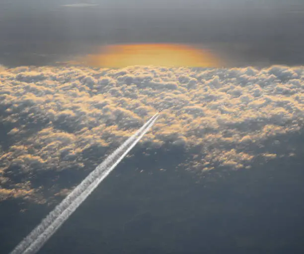 High angle view of passenger aircraft with vapour above the clouds at sunset