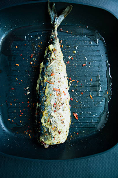 Fried mackerel in a grill pan, decorated with spices for fish. Dark background. View from above