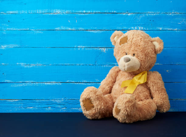 brązowy miś siedzi i żółtą jedwabną wstążką na niebieskim drewnianym tle, koncepcja walki z rakiem u dzieci - behavior teddy bear doll old zdjęcia i obrazy z banku zdjęć