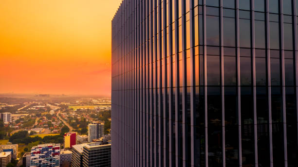 Side view of modern skyscraper teal and orange glassy facade with orange hazy sky, external building facade