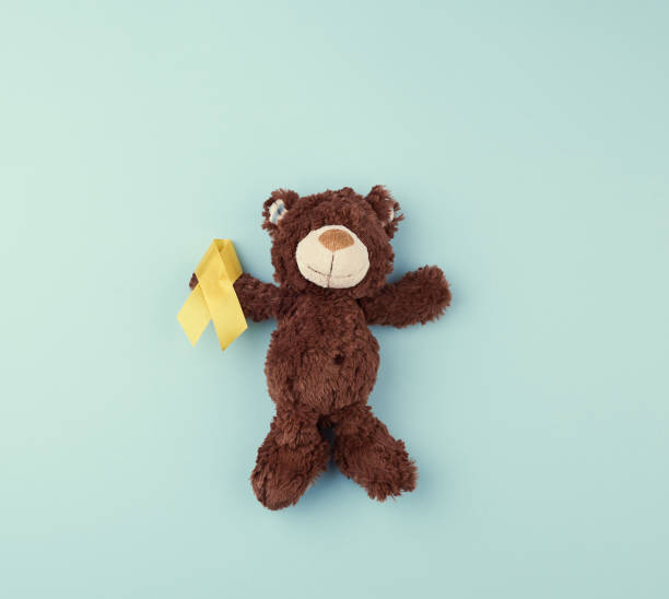 istock brown teddy bear holds in his paw a yellow ribbon folded in a loop on a blue background. concept of the fight against childhood cancer 1196896483