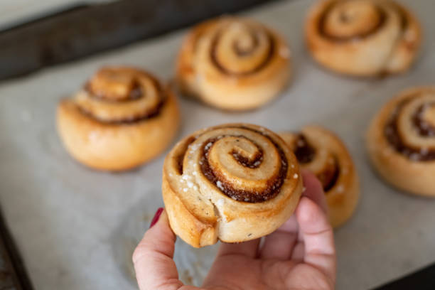 istock Hand taking freshly baked cinnamon buns rolls from a tray lined with baking parchment paper 1196902827