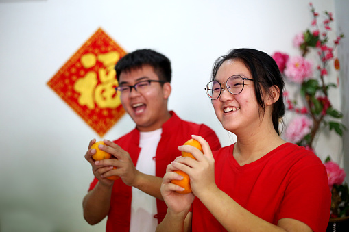 Malaysian teenage siblings are feeling joyful while holding mandarin oranges for Chinese New Year celebration.