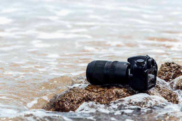istock DSLR camera on stone beach wet from water sea wave 1196923494