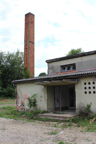 istock Entrance to old military barrack with broken windows and missing doors next to tall red brick chimney at abandoned military complex 1196940700