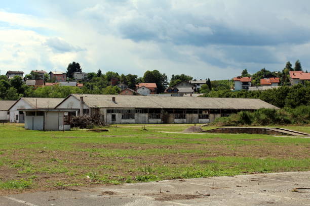 istock Elongated dilapidated military hangars with broken windows and destroyed walls surrounded with grass and family houses 1196940708