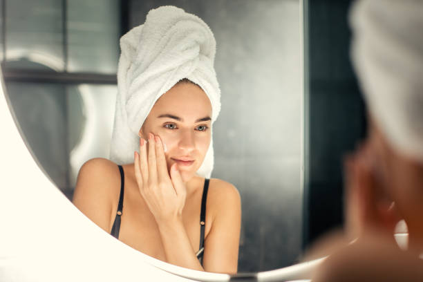 istock Young woman applying moisturizer in front of mirror 1196940862