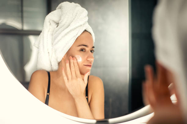 istock Young woman applying moisturizer in front of mirror 1196941472
