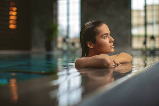 istock Beautiful young woman relaxing on indoors poolside 1196941473